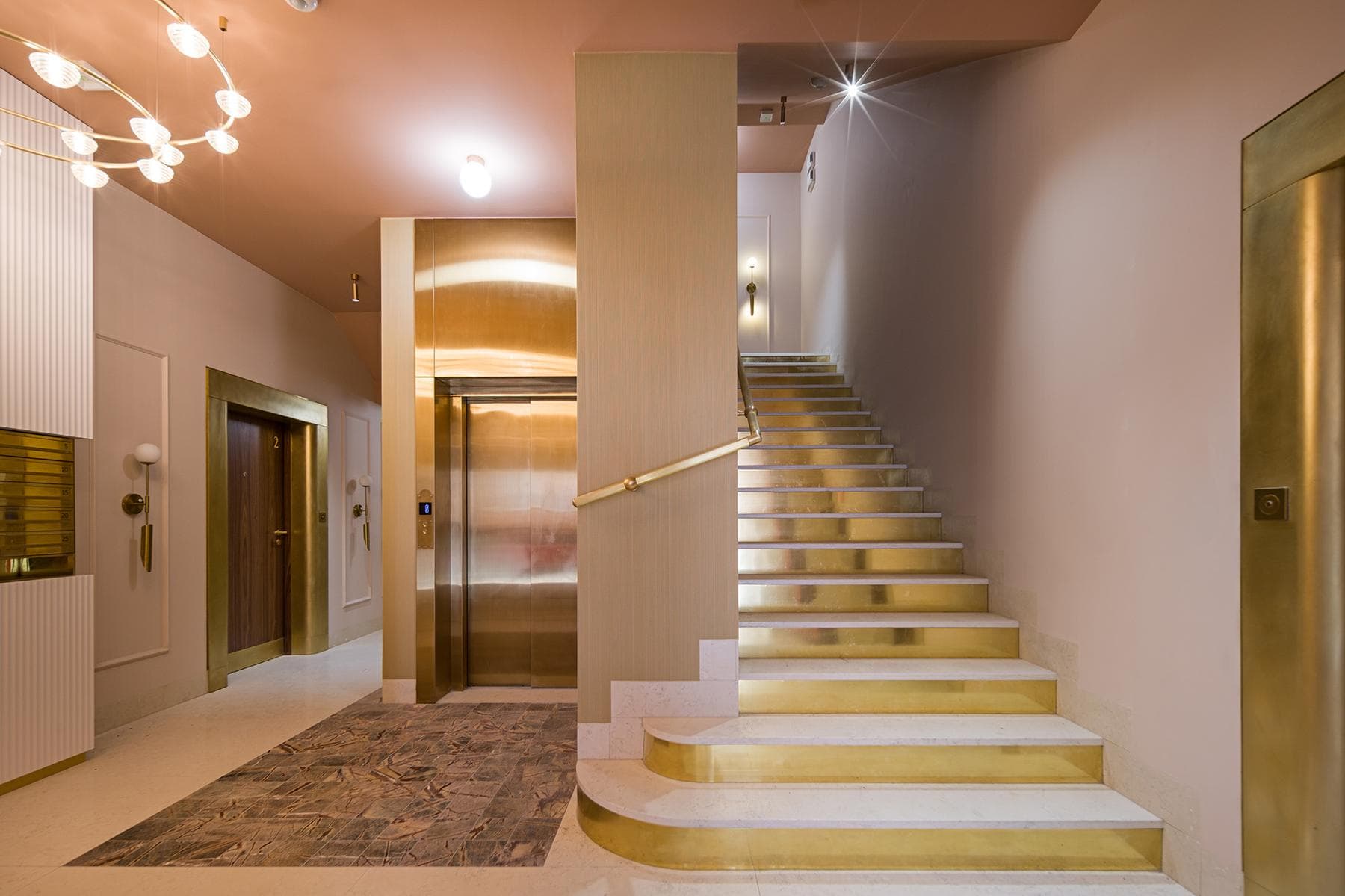 Lobby — mosiężne schody, żyrandol, złota winda